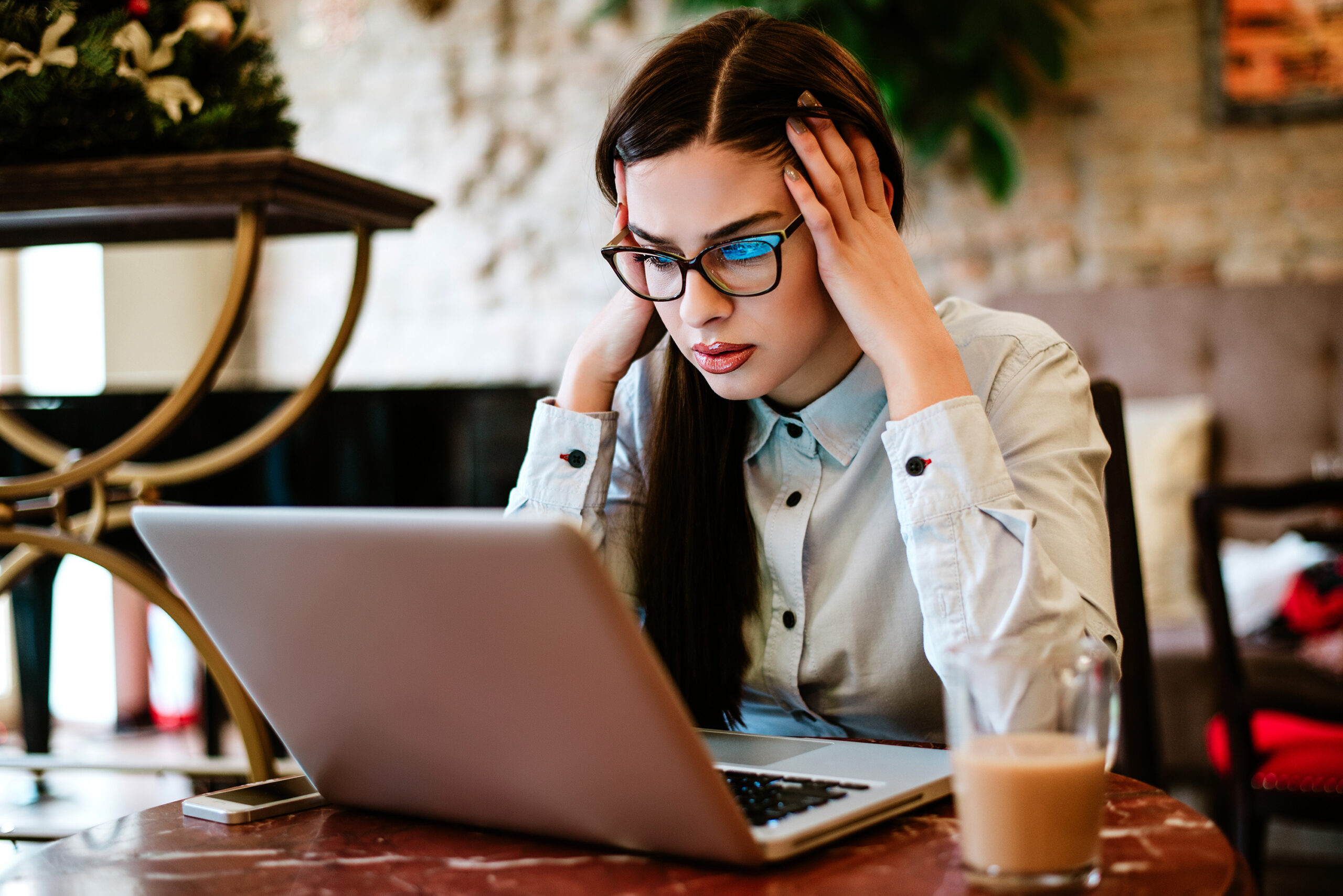 A woman frowning at a laptop screen, hands to her temples, struggling to find what she is looking for
